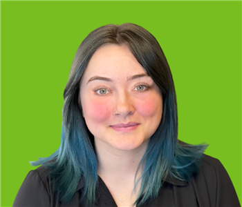 Female employee with black and blue hair smiling in front of a green background